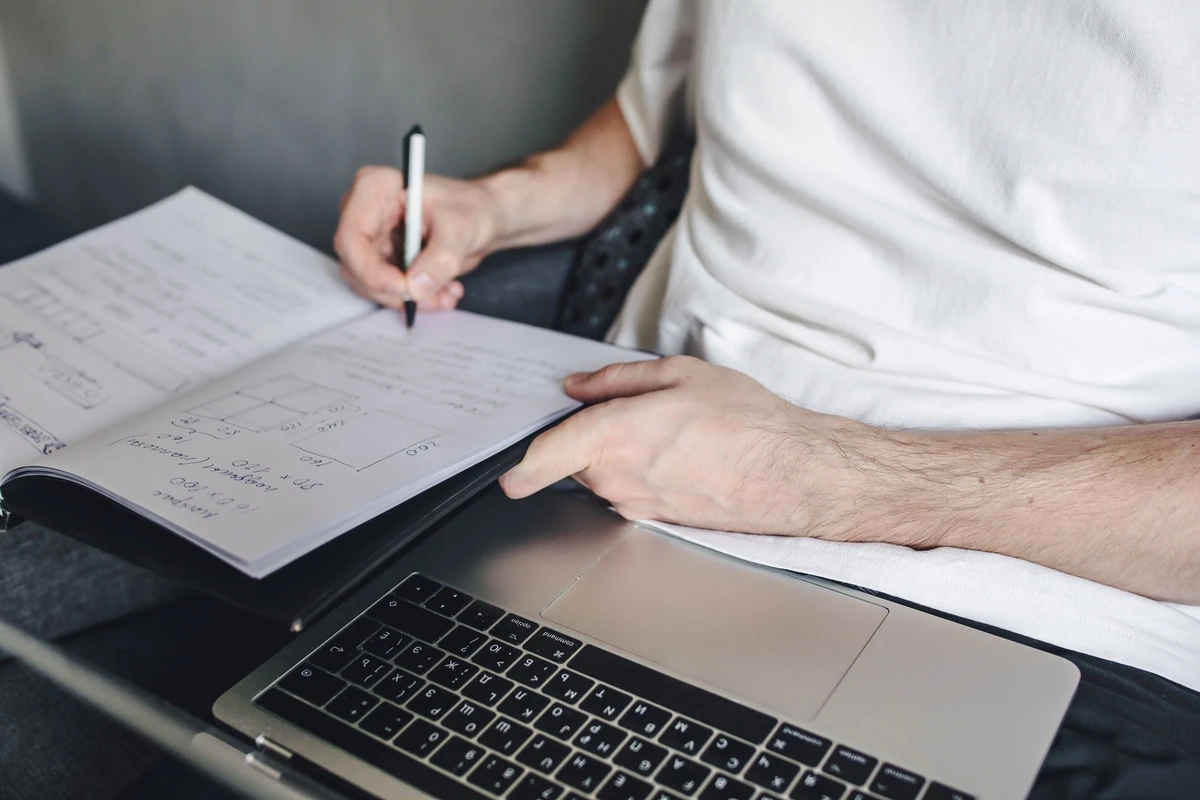 A person writing notes beside a laptop in an illustrative stock photograph