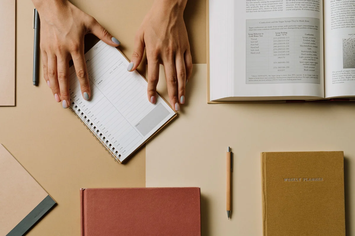 Hands arranging a notebook and books on a desk, illustrating the planning of availability rules