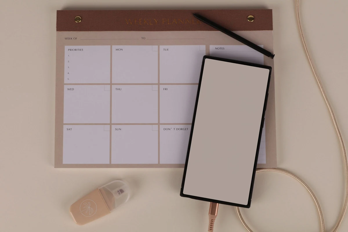 An unfilled weekly planner, blank phone screen and pen, illustrating the review of appointment changes