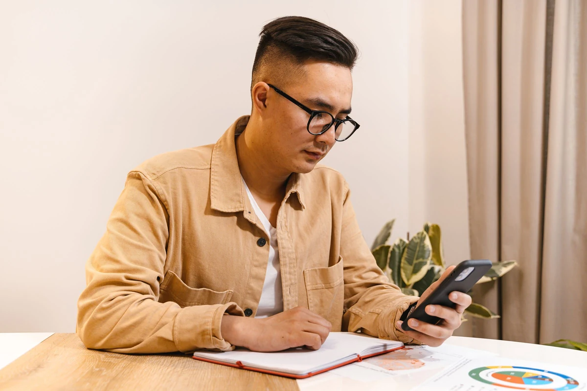 Office worker checking a smartphone beside a notebook, illustrating a receiving employee's review
