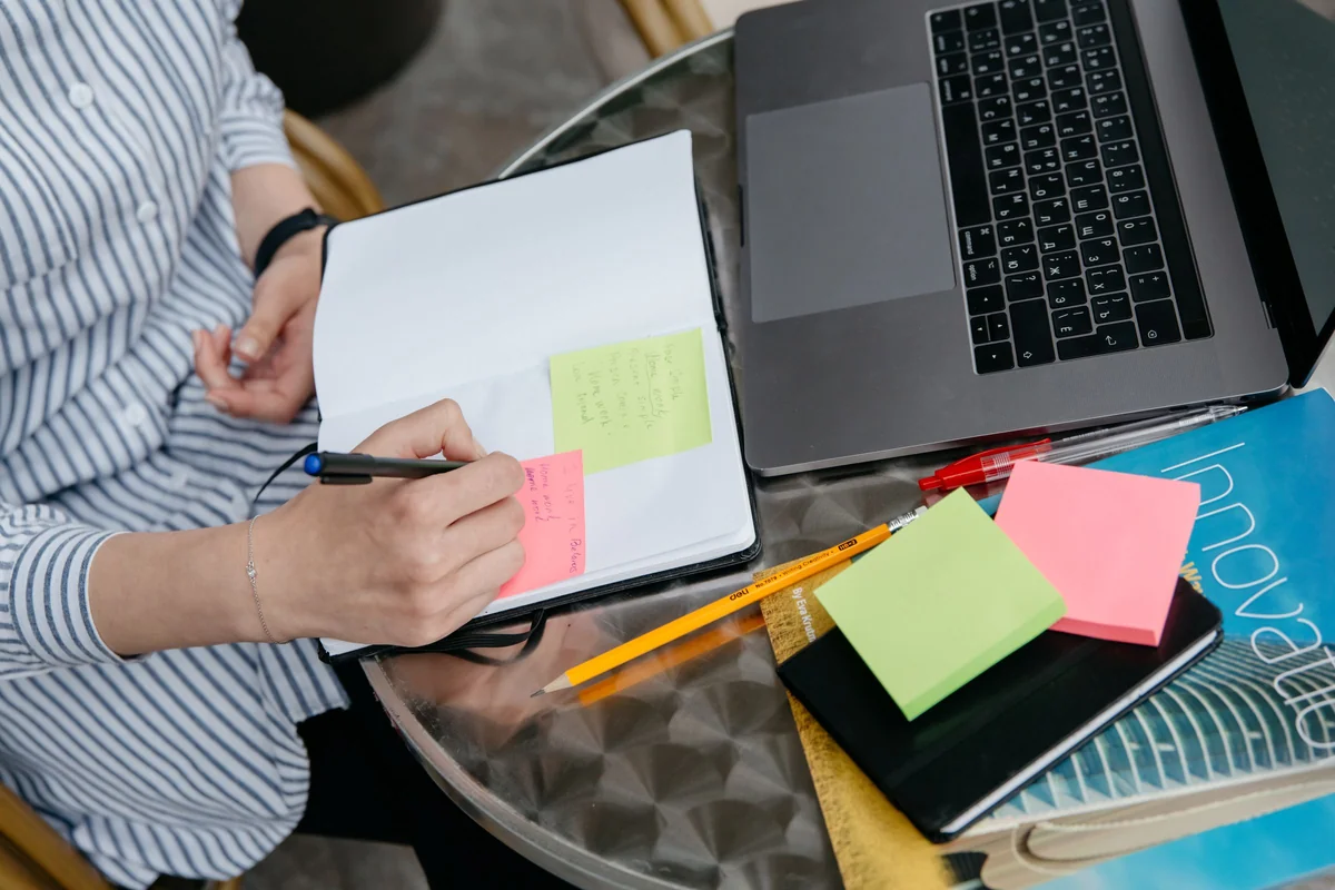 Person recording notes beside a laptop and sticky notes, illustrating review of website support actions