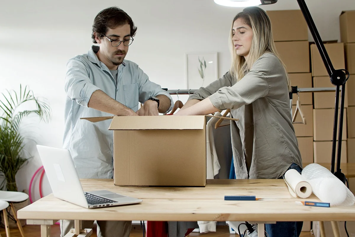 Two small-business operators packing a parcel beside a laptop, illustrating why payment verification must control fulfilment