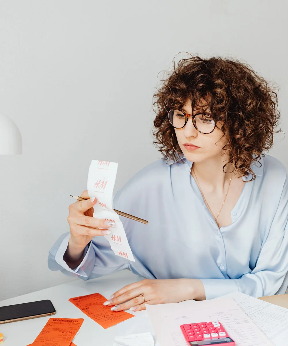 A woman reviewing a paper receipt with a calculator, illustrating refund and payment reconciliation