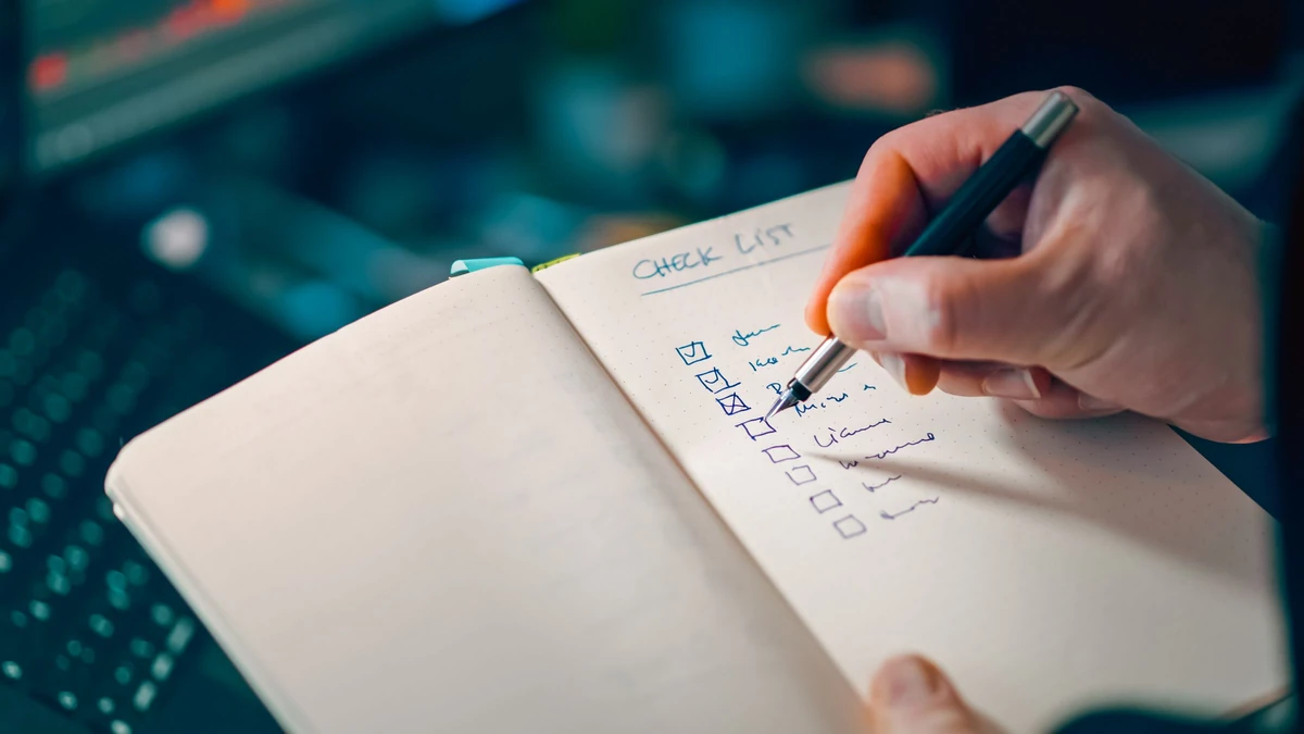 Hand writing a checklist in a notebook beside a keyboard, illustrating recording search acceptance checks