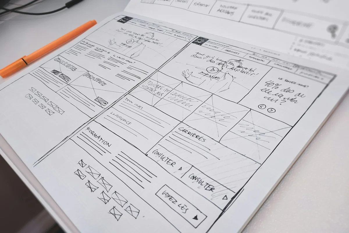 Hand-drawn website wireframe on paper with an orange pen, illustrating page planning